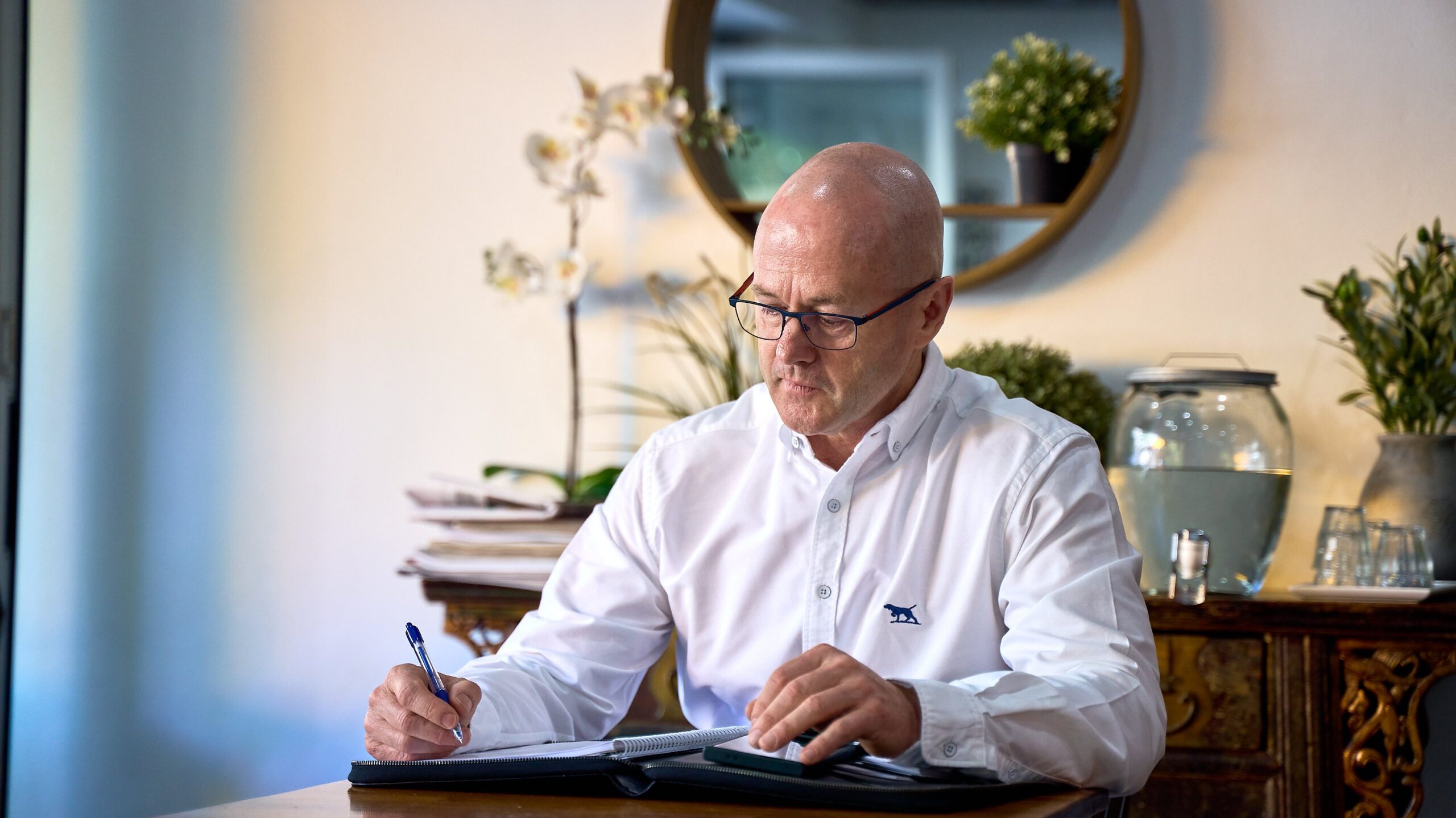 Michael Clapham sits at a table writing financial market updates in a compendium.